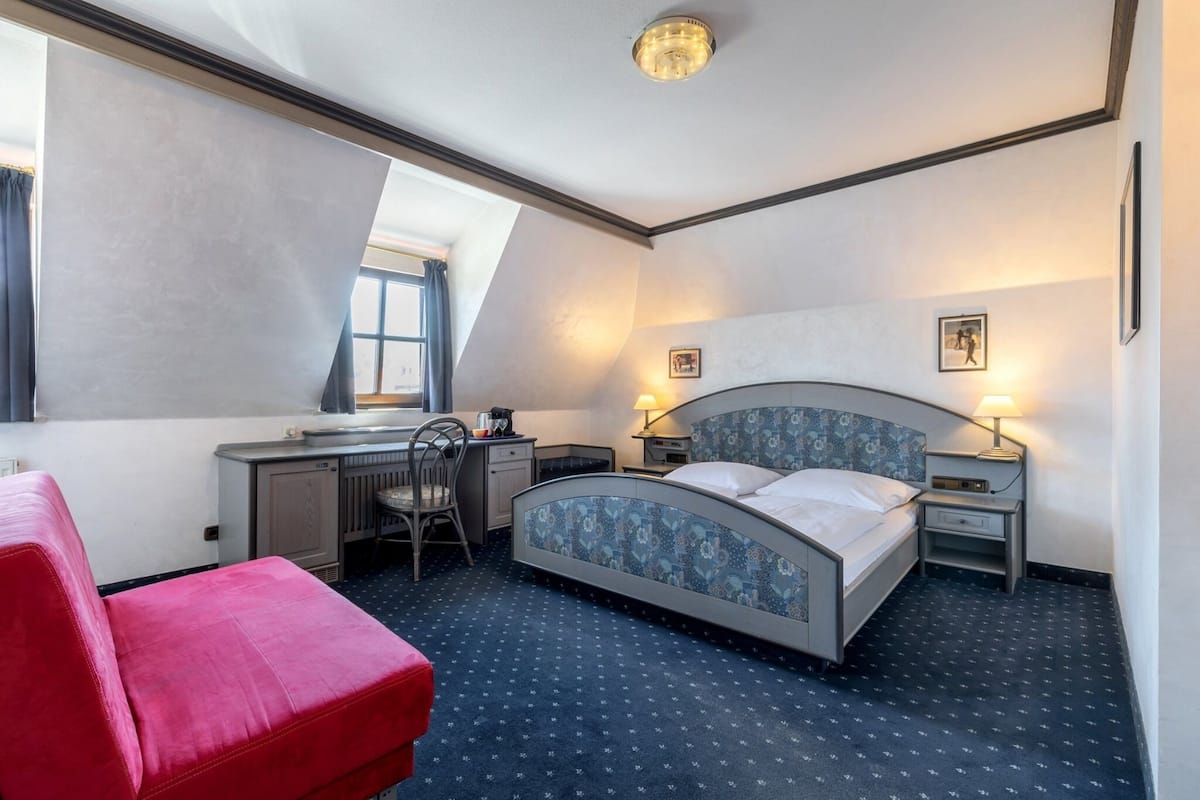 Une chambre d’hôtel avec un lit, un bureau, une chaise et un canapé rouge.