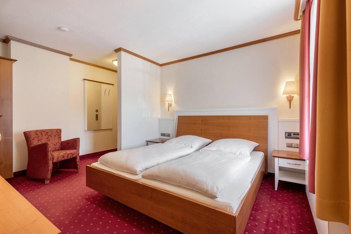 Une chambre d’hôtel avec un grand lit, une tête de lit en bois, des tables de chevet, une chaise et un miroir.