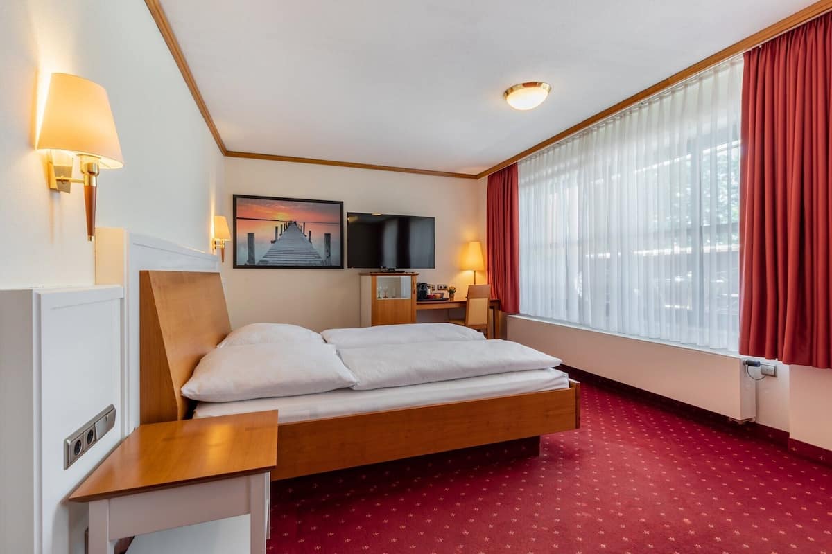 Une chambre d’hôtel avec un lit, des tables de chevet, une télévision, un bureau et une fenêtre avec des rideaux.