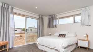A bedroom with a large bed, a nightstand, a lamp, and a view of the outdoors through a sliding door.