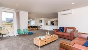 A modern living room with a brown leather sofa, a wooden coffee table, and a dining area with a wooden table and chairs.