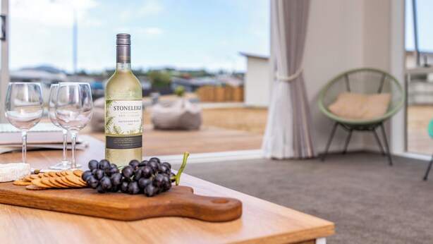 A wine bottle on a table with glasses and grapes, a chair, and a view of the sky.