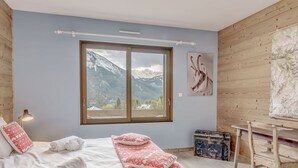 Un dormitorio con un ventanal grande, una cama con ropa de cama blanca y roja, un escritorio y una silla.