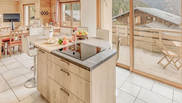 Una cocina moderna con una isla grande, armarios de madera y vistas a un paisaje montañoso a través de puertas correderas de vidrio.