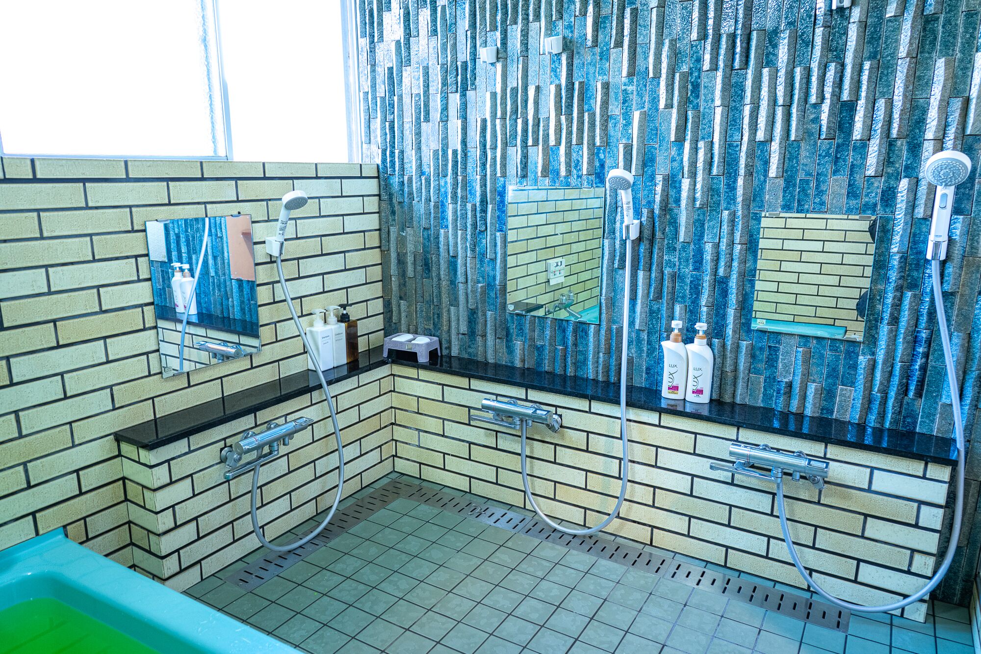 A bathroom with a tiled wall, a mirror, a sink, and a shower area.