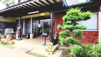 A building with a covered entrance, a brick wall, and a well-maintained garden with potted plants and a bonsai tree.