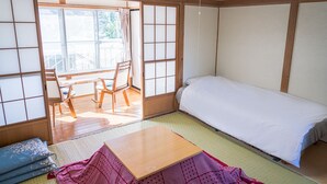 A traditional Japanese room with tatami flooring, a low wooden bed, a small table, and a sliding door leading to an outdoor area. - Ryokan Fuji Heights (Fujikawaguchiko)