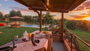 Une terrasse extérieure avec une table dressée pour le dîner, une piscine et une vue imprenable sur le coucher de soleil.
