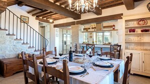 Un coin repas avec une table dressée pour le repas, des chaises en bois, un lustre et un mur en pierre.
