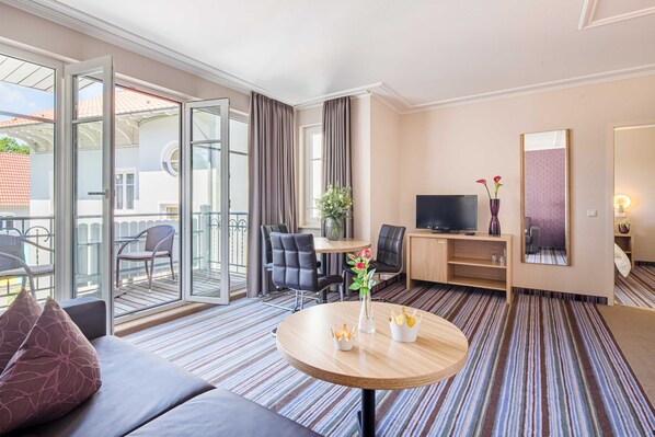 Habitación de hotel con sofá, una mesa redonda con un florero, televisor, escritorio y silla.