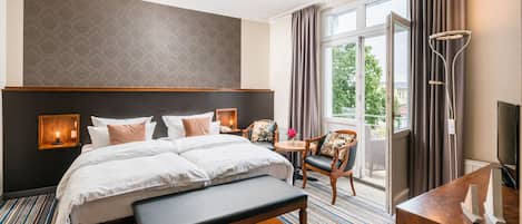 A hotel room with a large bed, a desk, a chair, a bench, a TV, and a balcony with curtains.
