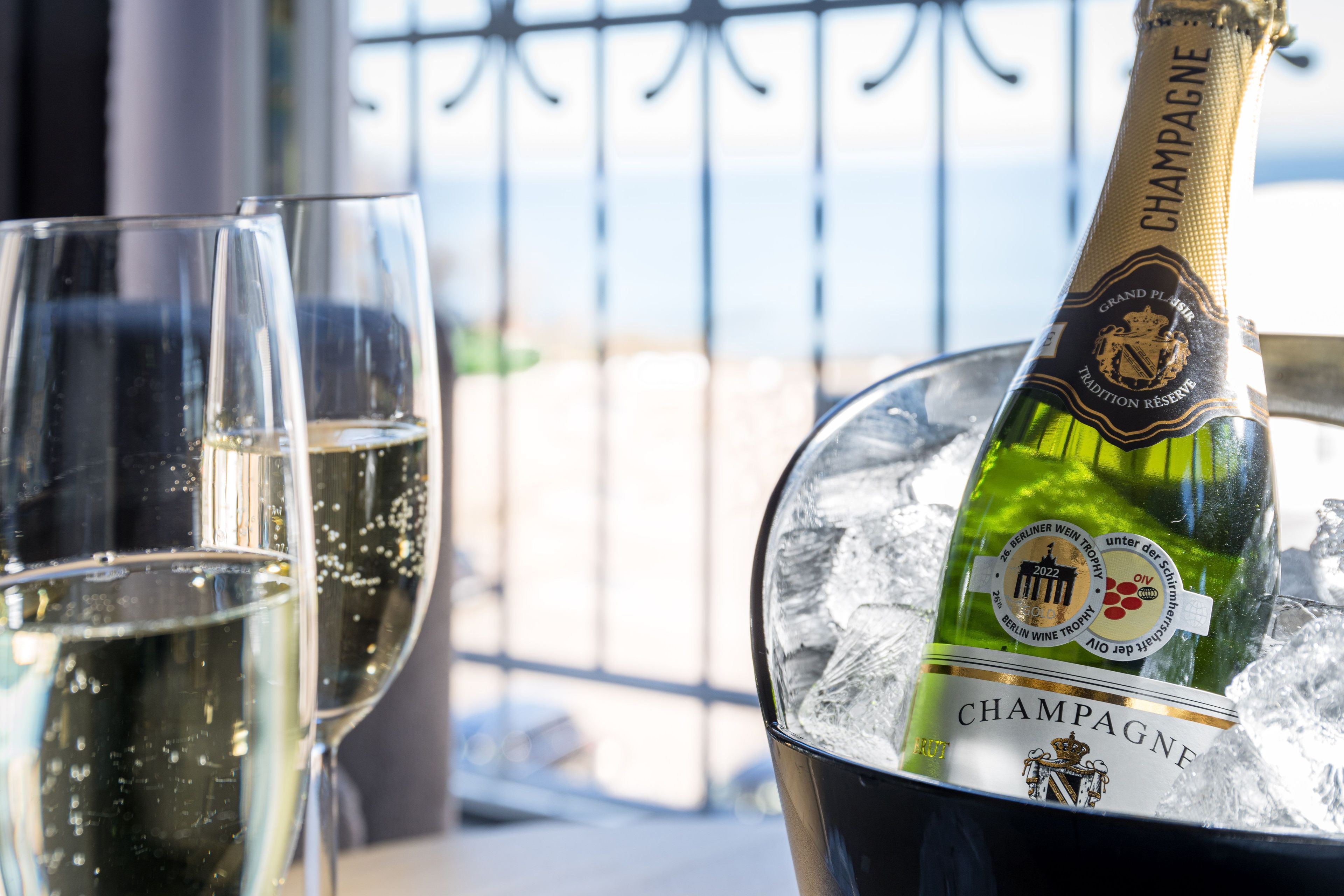 A bottle of champagne in an ice bucket with two glasses beside it.
