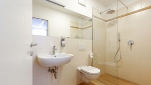 Een moderne badkamer met een wit wastafelmeubel, toilet en douchecabine met glazen wanden.
