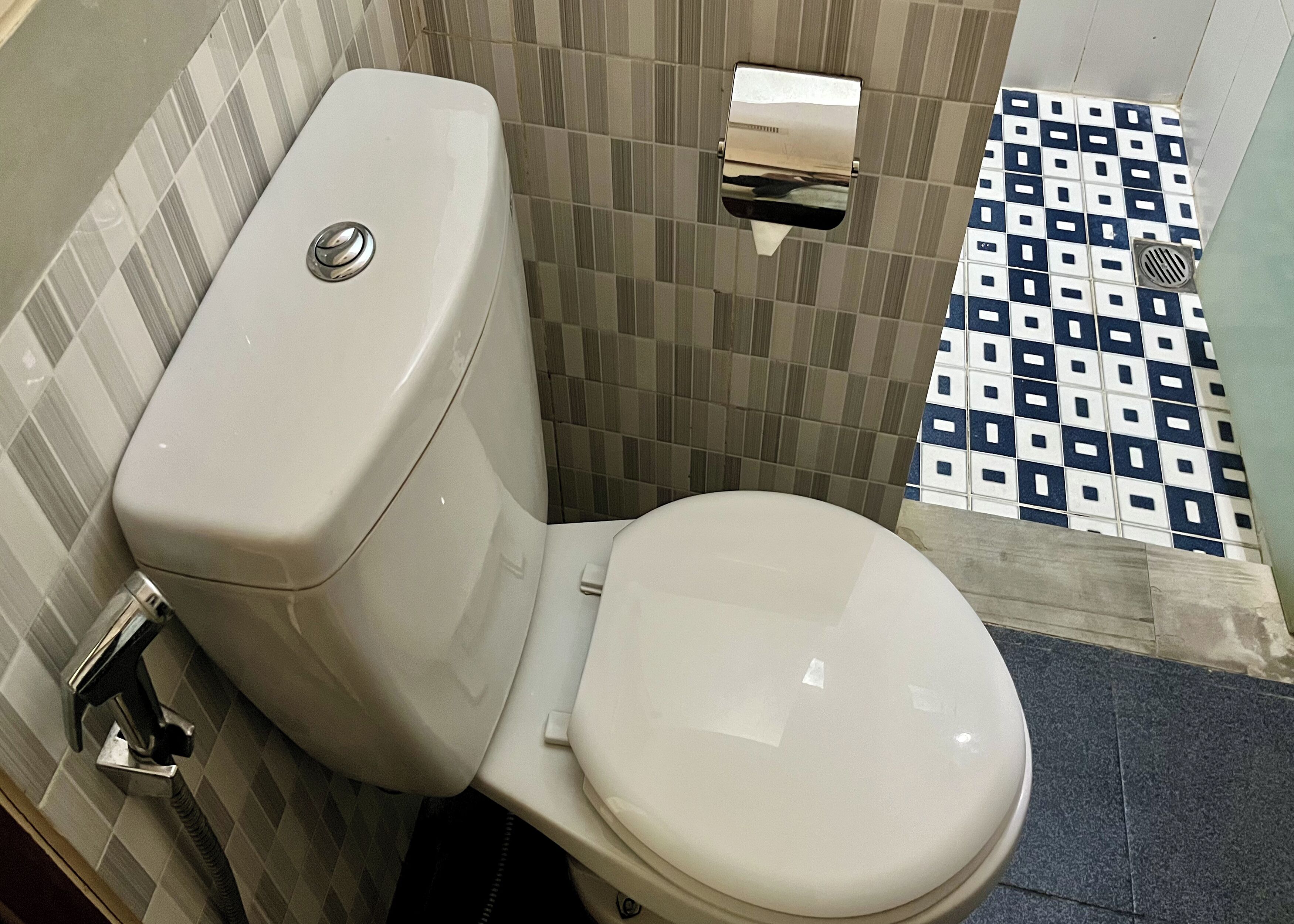 A toilet with a white tank and seat, a paper towel dispenser, and a floor with a checkered tile pattern.