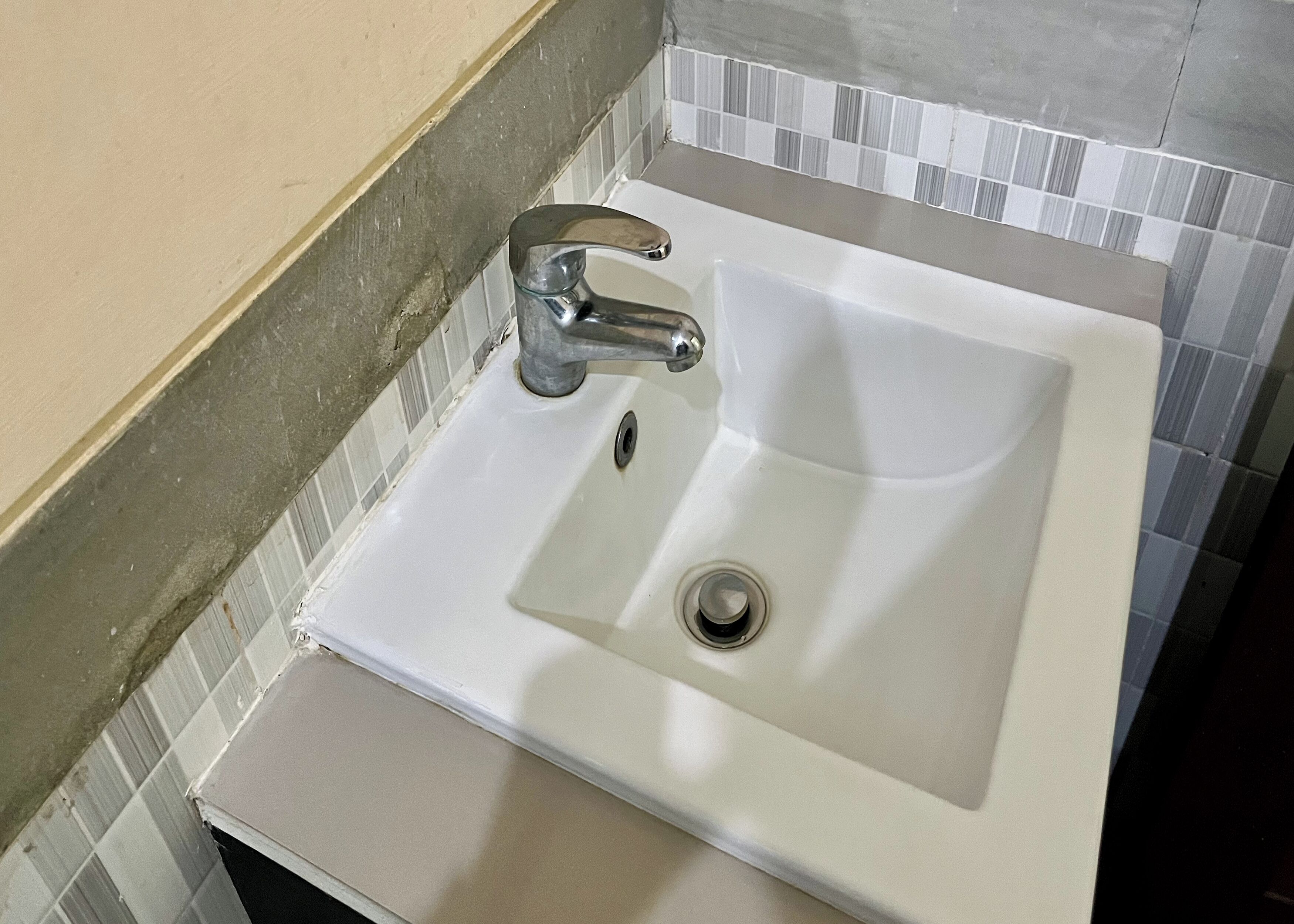 Un lavabo de salle de bain avec un robinet chromé, un drain et un pare-éclaboussures carrelé.