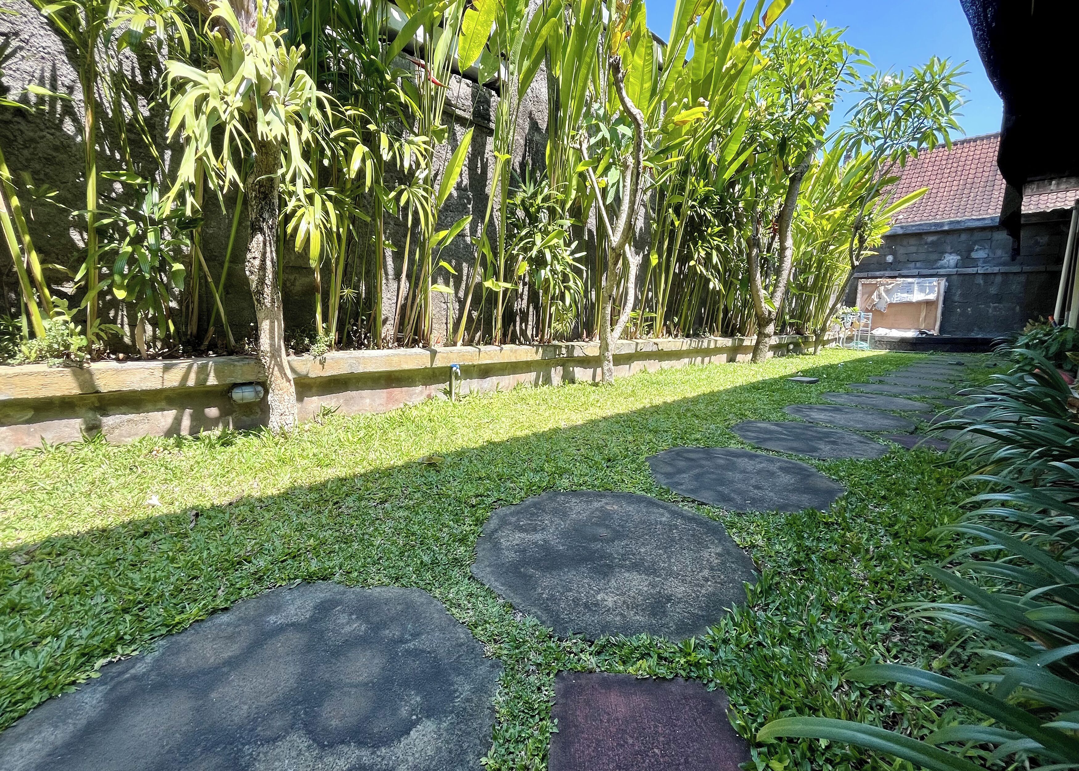 A garden pathway with stepping stones, lush greenery, and a stone wall.