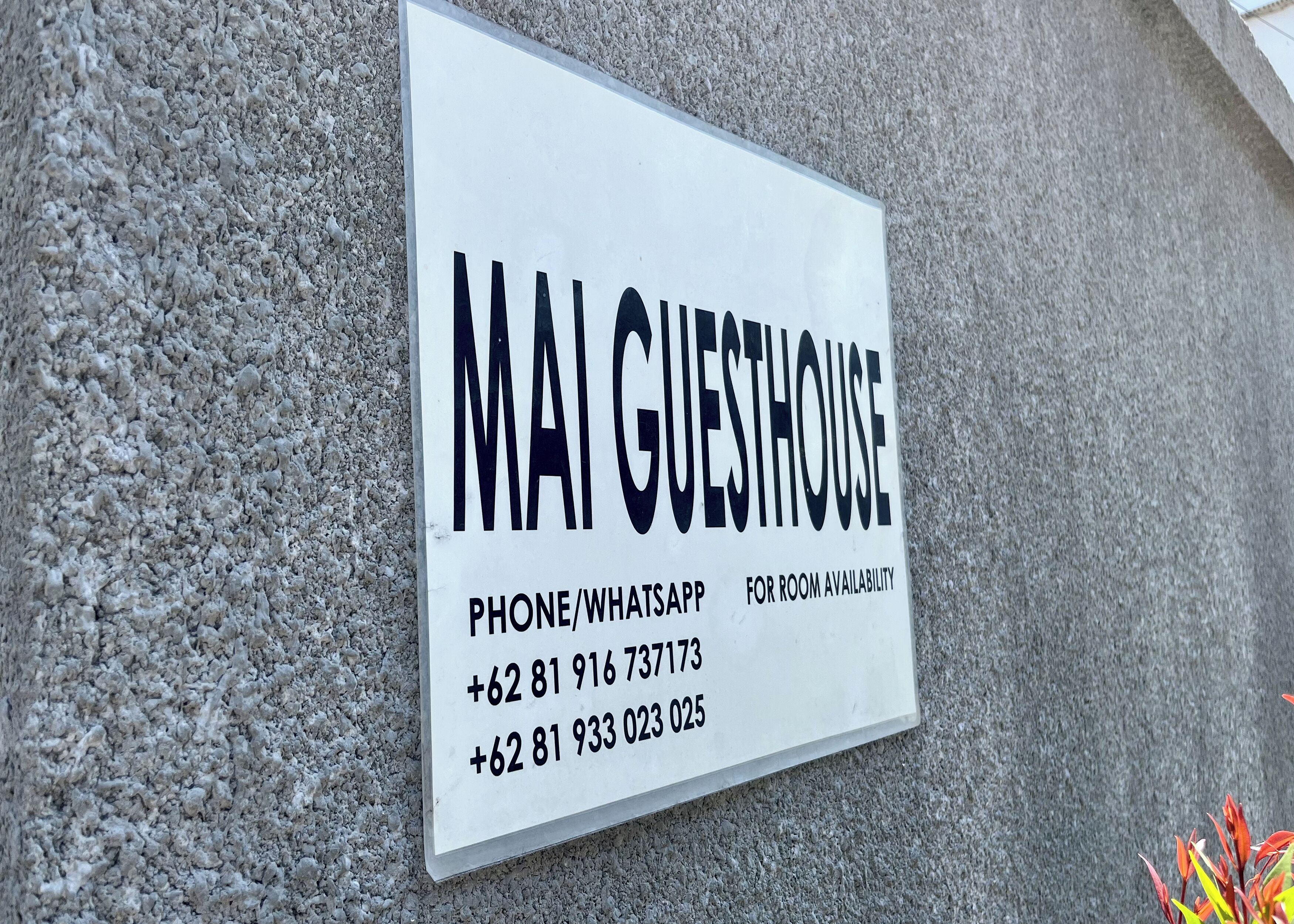 A sign for Mai Guesthouse with contact numbers for room availability.