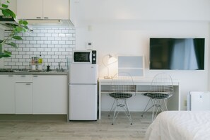 Een moderne keuken met witte kasten, een magnetron en een koelkast. Er is een bureau met twee stoelen en een televisie aan de muur bevestigd.