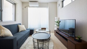 Uma sala de estar moderna com sofá, mesa de centro, televisão e uma janela ampla com persianas.