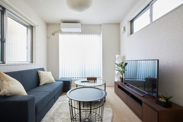 A modern living room with a sofa, a coffee table, a TV, and a large window with blinds.