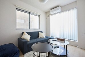 A modern living room with a dark blue sofa, two white cushions, a glass coffee table, and a small side table.