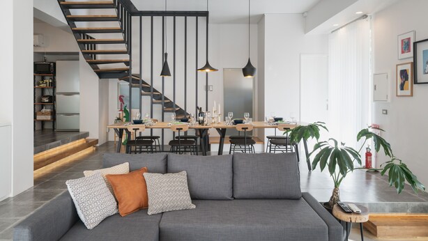 A modern living room with a grey sofa, a wooden staircase, and a dining area with a wooden table and chairs. - Infinity Hotel -Higawa- (Naha)