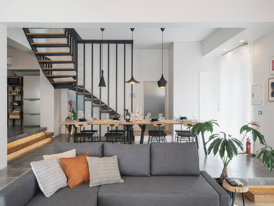 Un salon moderne avec un canapé gris, un escalier en bois et un coin repas comprenant une table et des chaises en bois.