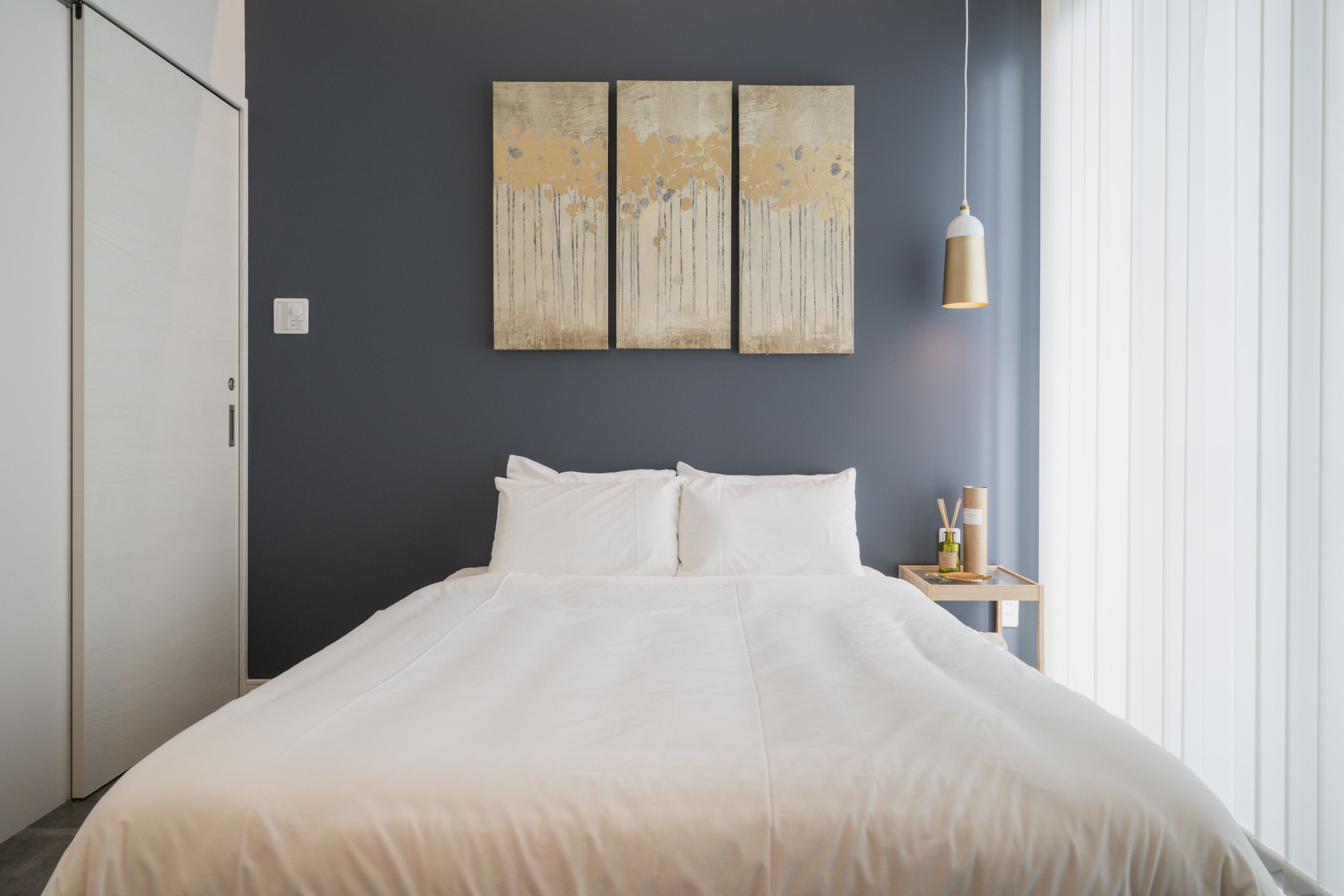 A bedroom with a large bed, a nightstand with a lamp, and a wall-mounted artwork.