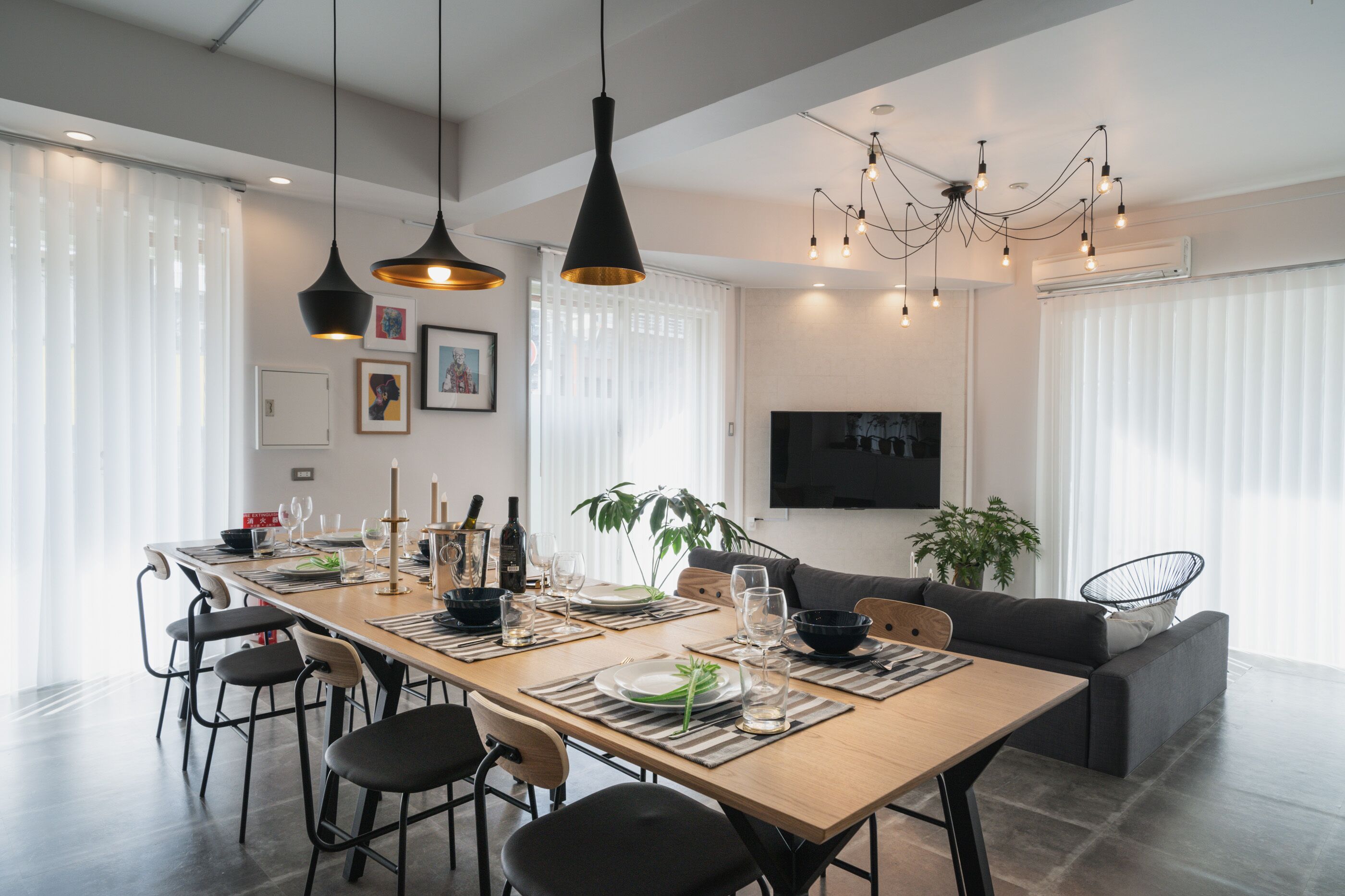 A modern dining area with a long table, multiple chairs, and hanging pendant lights.