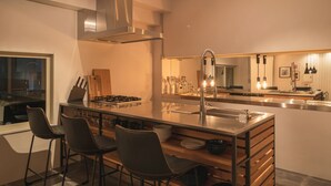 A modern kitchen with a central island, bar stools, stainless steel appliances, and a large mirror. - Infinity Hotel -Higawa- (Naha)