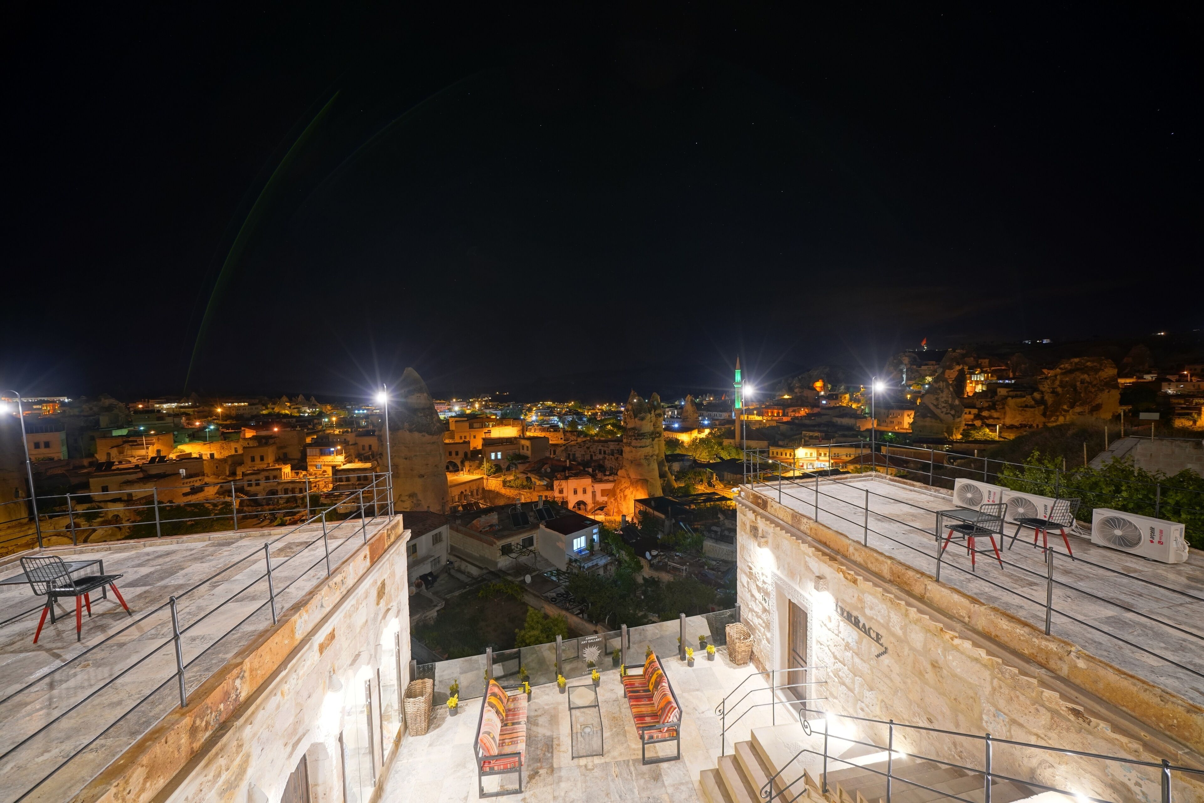 A rooftop terrace with seating and a view of a cityscape at night.