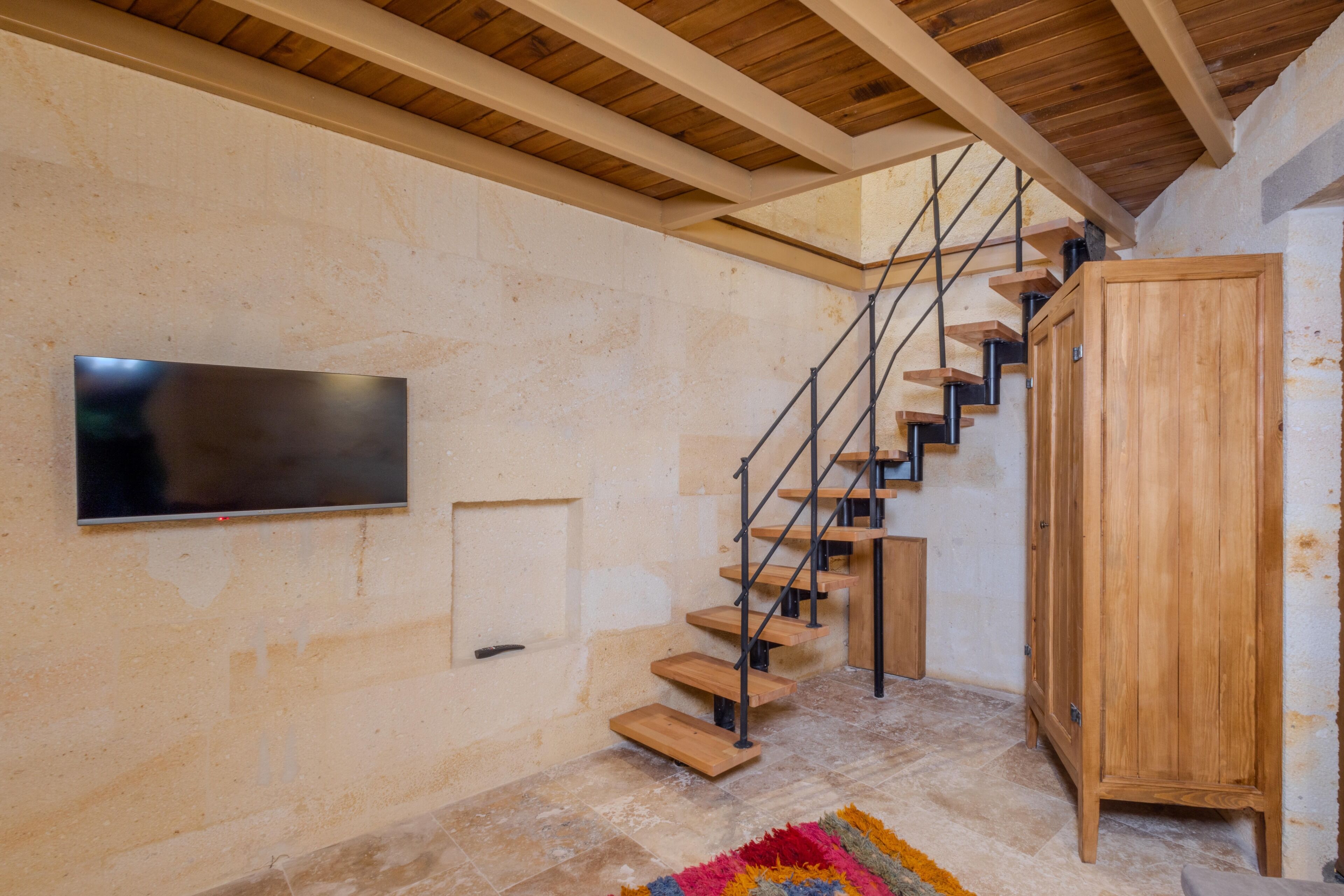 Una escalera con escalones de madera y barandillas metálicas, un armario de madera y un televisor de pantalla plana montado en la pared.