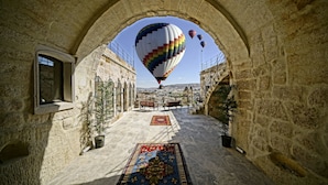 A stone corridor with a large archway, leading to a view of a cityscape and a hot air balloon in the distance. - Arinna Cappadocia (Nevsehir)