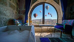A room with a large arched window, a bathtub, a table, and two chairs. - Arinna Cappadocia (Nevsehir)