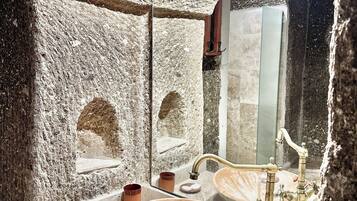A bathroom with a stone wall, a large mirror, and two sinks with vintage faucets.