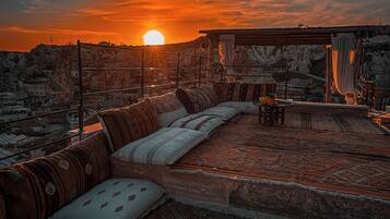 A sunset view from a rooftop terrace with a sofa and cushions, a hanging chair, and a view of the cityscape.