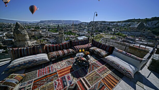 A rooftop terrace with colorful textiles, a dining area, and a view of a cityscape with hot air balloons. - Arinna Cappadocia (Nevsehir)
