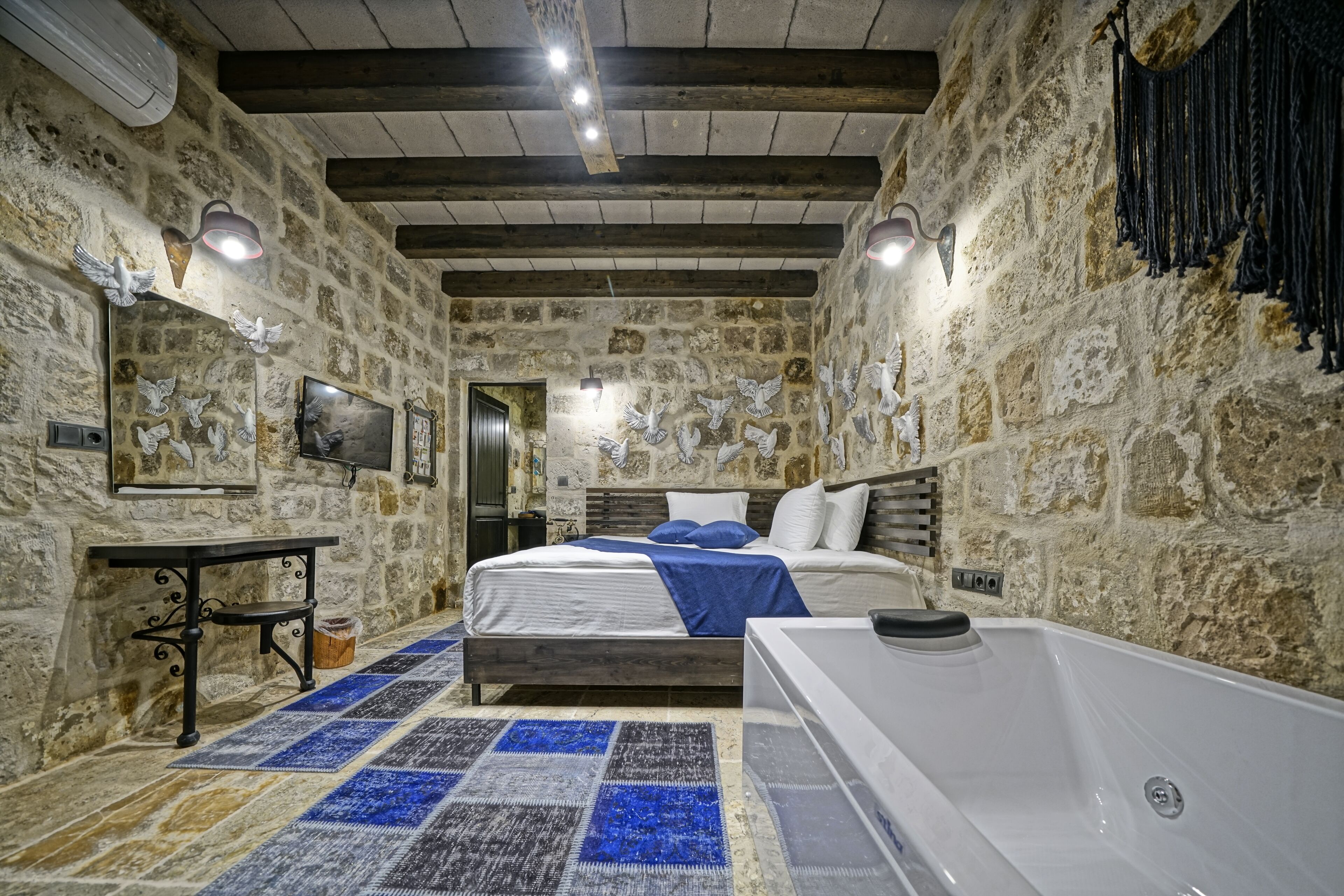 Un dormitorio con paredes de piedra, una cama, una mesita, un banco y una bañera.