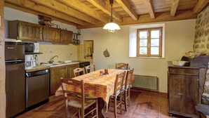 A rustic kitchen with wooden beams, a dining table with chairs, a stove, and a refrigerator.