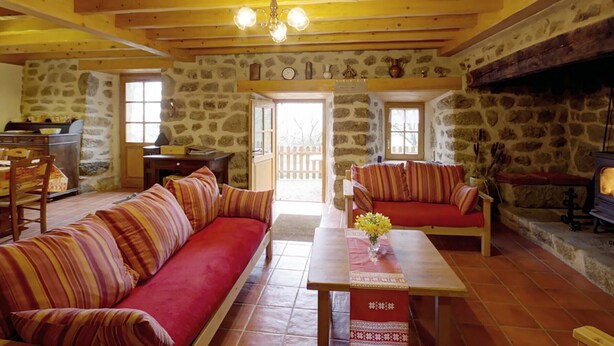 A cozy room with a wooden ceiling, stone walls, a sofa set, a dining table, and a fireplace.