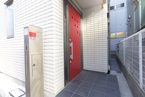 Esterno di un edificio con una porta rossa, un armadietto beige e un muro di mattoni bianchi.