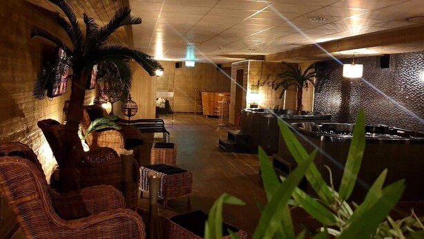 A spacious lobby with wicker furniture, a bar area, and decorative palm plants. - Hotell Pausa (Klippan)