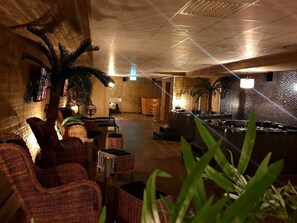 A spacious lobby with wicker furniture, a bar area, and decorative palm plants. - Hotell Pausa (Klippan)