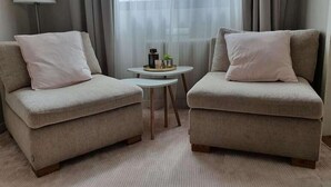 A room with two beige armchairs, a small round table with a lamp, and sheer curtains. - Hotell Pausa (Klippan)