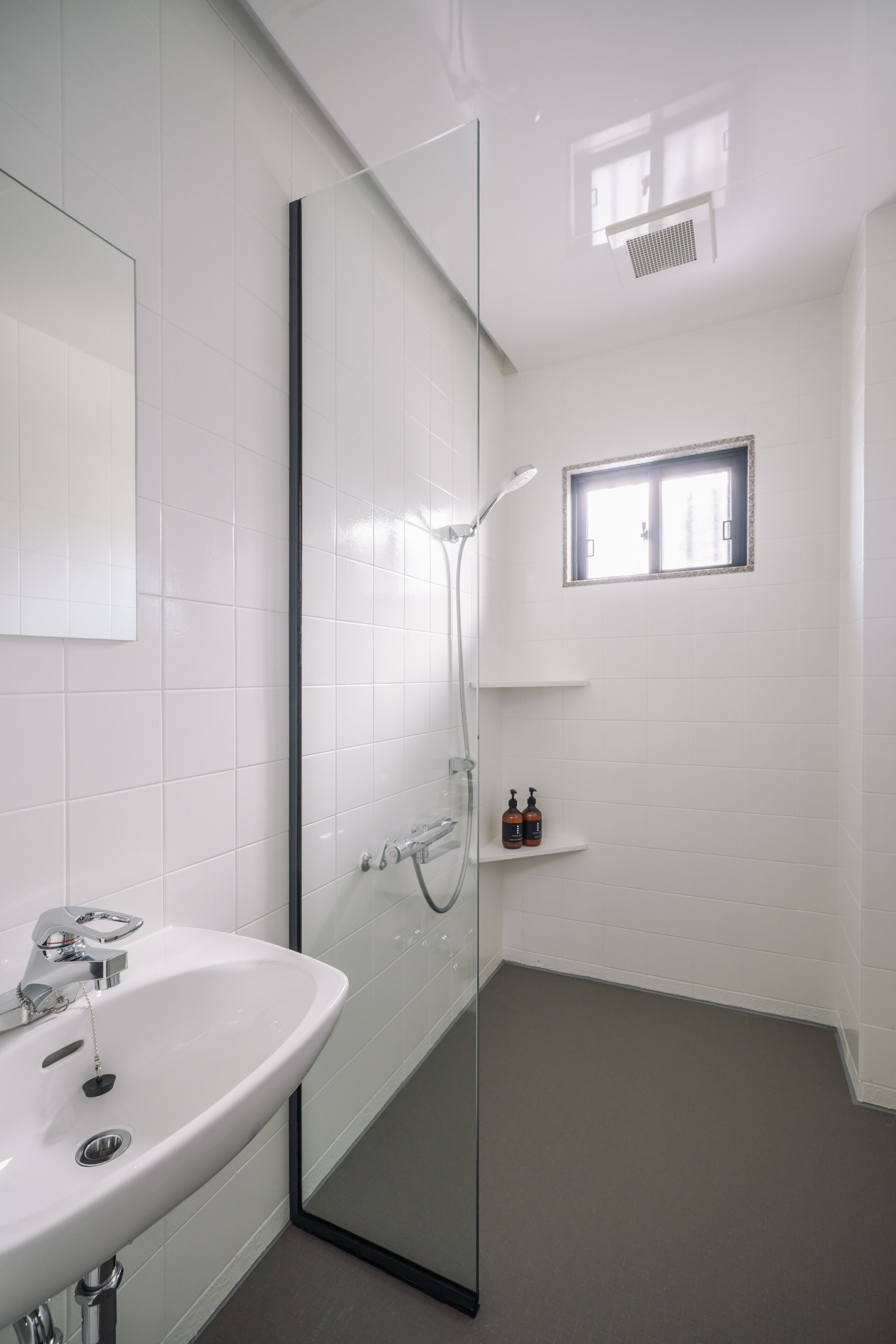 A modern bathroom with a glass-enclosed shower, a white sink, and a small window.