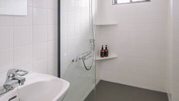 A modern bathroom with a glass-enclosed shower, a white sink, and a small window.