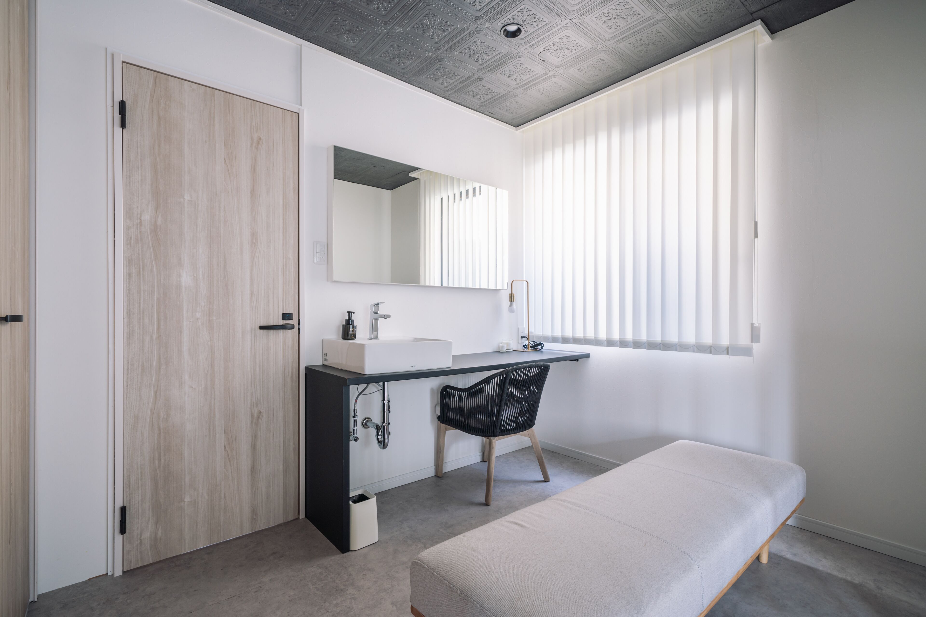 Un baño moderno con puerta de madera, un lavamanos blanco, un espejo y un banco.