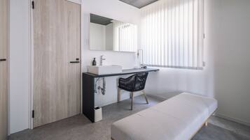 Un baño moderno con puerta de madera, un lavamanos blanco, un espejo y un banco.