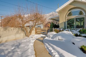 Stroll along the snow-covered pathway to this modern home, featuring a large arched window and garage door.