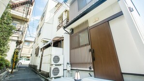 A narrow urban street with residential buildings, air conditioning units, and a wooden gate. - Oyado Toshi (Kyoto)